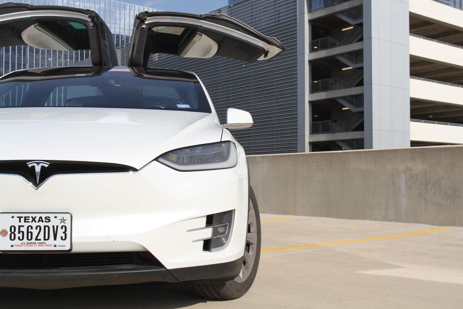 Front of a white Tesla Model X with its falcon doors open in a parking structure
